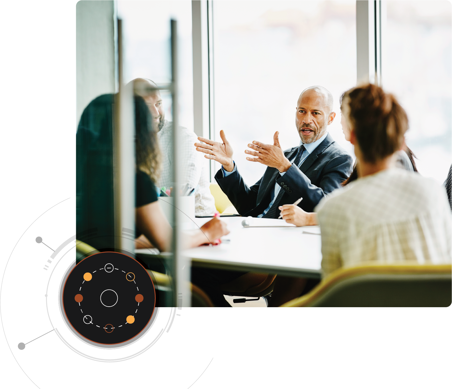 Un uomo parla a diverse persone sedute intorno a un tavolo da conferenza, con l'immagine di un cerchio sovrapposto nell'angolo in basso a sinistra.